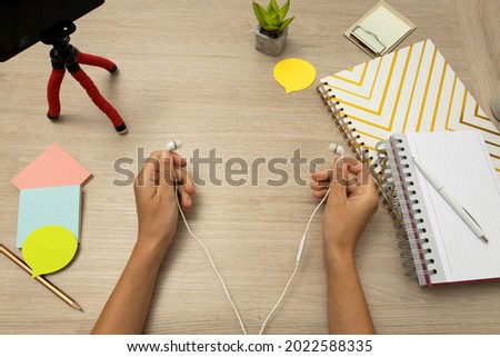 Woman holding white earphones, notebooks, papers and smartphone, tripod on the wooden table.Concept of home learning or video streaming