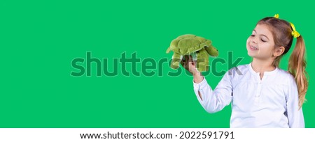 Nice pretty young girl holding a soft toy turtle green color and looking at it with a smile.