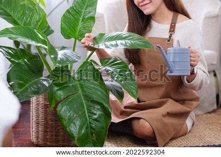 Closeup image of a beautiful young asian woman taking care and watering houseplants by watering can at home