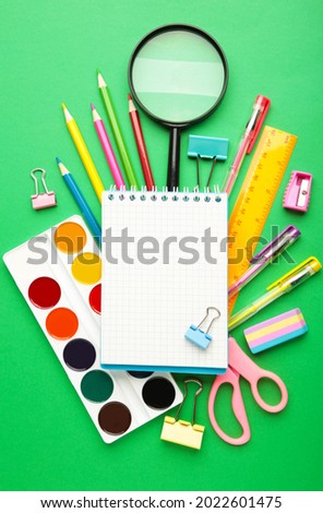 Notebook with stationary objects on green background. Vertical photo. Top view