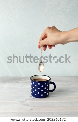Dark blue mug  polka dots with cocoa on wooden table. Woman's hand is stirring cocoa with a small spoon. Background with copy space for your text. Close up. Vertical. Toned
