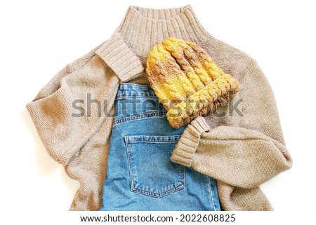 Brown woolen sweater, blue jeans and yellow knitted hat. Fall and winter fashion outfit flat lay photography