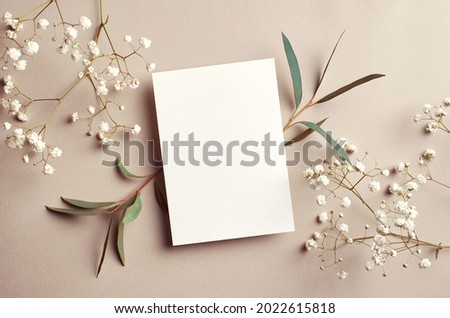 Wedding invitation card mockup with natural eucalyptus and white gypsophila twigs. Blank card mockup on beige background. Royalty-Free Stock Photo #2022615818