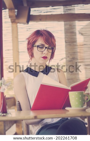 Cute hipster teenage girl reading a book and enjoying coffee