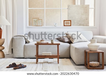 Creative composition of stylish and cozy living room interior with mock up frame, grey corner sofa, window, coffee tabels and personal accessories. Beige neutral colors. Template.