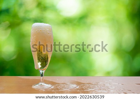 Beer bubbles overflowing from a glass placed on a wooden bar.