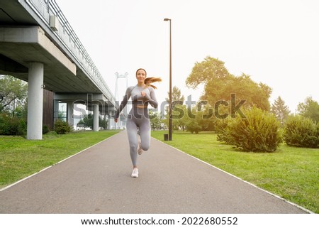 Woman dressed leggings and top running asphalt road summer park. Healthy lifestyle concept. Active and athletic female exercises outdoor
