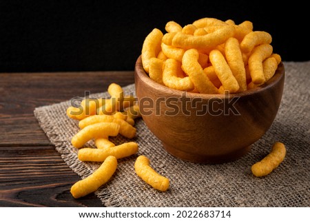 Cheese flavored puffed corn snacks on wooden background. Royalty-Free Stock Photo #2022683714