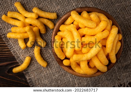 Cheese flavored puffed corn snacks on wooden background. Royalty-Free Stock Photo #2022683717