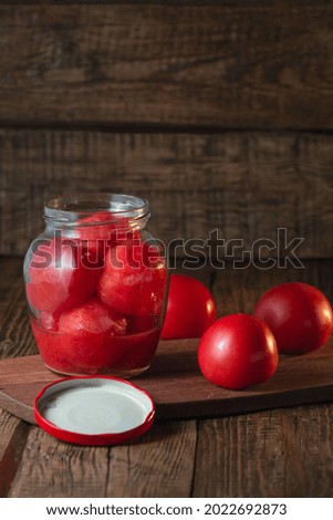 There is a glass jar with red tomatoes on a wooden stand. Preservation, salting of vegetables. Brown background, copy space, vertical orientation.