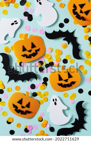 Halloween party concept with fun paper decor, pumpkins, ghost and bat on blue background, top view