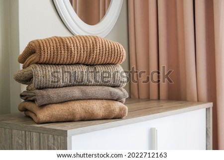 Stack of clean freshly laundered, neatly folded women's clothes on bedroom dresser's top. Pile of different sweaters of pastel colors in stack. Copy space, close up, background.