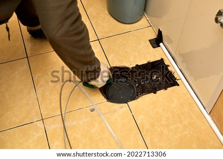 Sewer cleaning. A plumber uses sewer snake to clean blockage clog. Toilet room repair. Canalization pipe. Repairman hands. Bad smell. Dirty water. Metal wire. Yellow color tiles. Plumbing error. DIY. Royalty-Free Stock Photo #2022713306