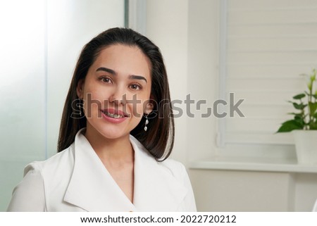 Portrait of beautiful smiling brunette nurse or doctor wearing white coat