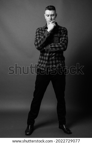 Studio shot of young handsome man wearing checkered shirt against gray background in black and white