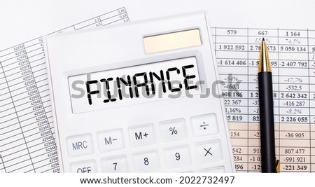 On the desktop there are reports, a white calculator with the text FINANCE on the scoreboard and a pen. Business concept.