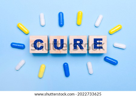 On a light blue background, multicolored pills and wooden cubes with the text CURE. Medical concept