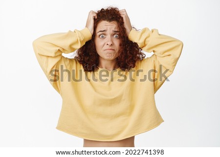 Freak out redhead girl looking distressed, having big mindblowing problem, holding hands on head and stare hopeless troubled at camera, white background