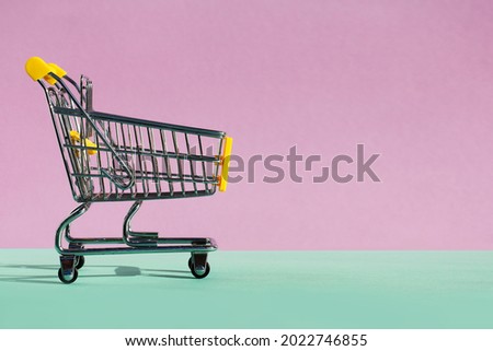 Small supermarket grocery push cart for shopping toy with wheels on violet-green background. the concept of consumption, in-store purchases, sales