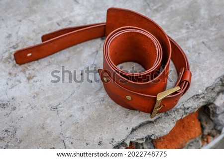 Handmade genuine leather strap for guitar. Beautiful orange leather products with a brass buckle. Natural old background for subject shooting. Horizontal photo.