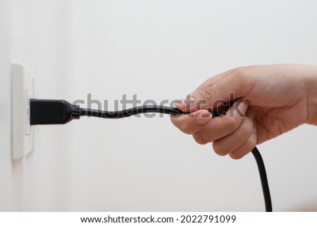 A woman's hand is pulling the power cord in a wrong design. Risk of danger and damage to the power plug, power cord. Royalty-Free Stock Photo #2022791099