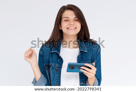 Happy satisfied girl in casual wear holding mobile phone, isolated over blue background