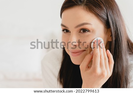 Young beautiful woman using applying cream softening moisturizer with cotton pad on her face, removing cosmetics. Beauty treatment, skin body care. Rejuvenation concept Royalty-Free Stock Photo #2022799613