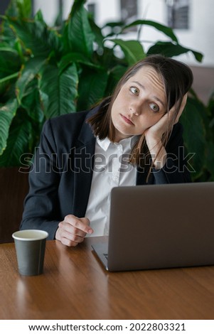 sad business woman with dark short hair working at the computer and bored, work in an office or at home, co-working or public place in a coffee shop. work at a laptop, monotonous and boring activities