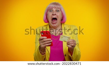 Senior stylish granny woman using credit bank card and smartphone while transferring money, purchases online shopping, found out great big win news doing winner gesture. Elderly grandmother pensioner