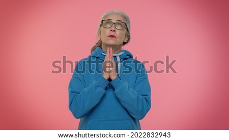Please, God, forgive me. Mature old granny woman praying, looking upward and making wish, asking for help with hopeful imploring expression, begging apology. Senior grandmother on pink background