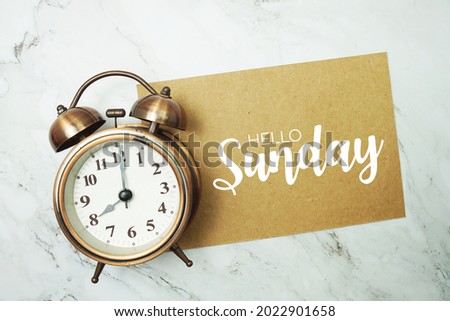 Hello Sunday typography text on paper card with alarm clock on marble background