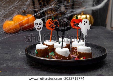  Sweet Halloween treat, chocolate covered marshmallows with sugar and Halloween decorations on a black plate, photo with soft focus