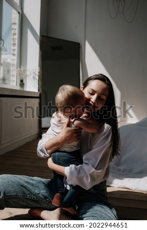 a happy brunette mom and a baby girl are sitting on a wooden floor in the rays of light