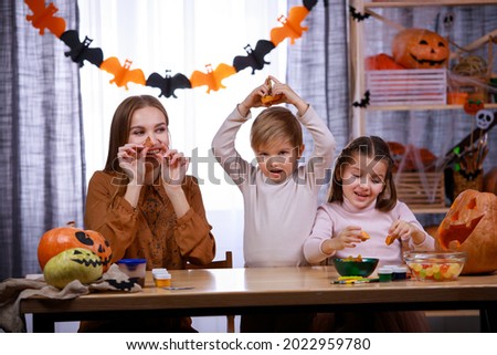 Happy family is preparing for Halloween at home. Mom, daughter and son are sitting at the table and playing with carved pumpkin cutters. Happy family party at home. Close up.