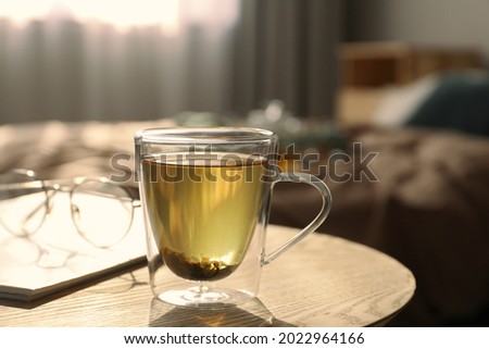 Glass cup of freshly brewed tea on wooden table in bedroom. Cozy home atmosphere