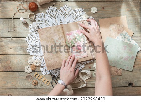 Scrapbooking. On a wooden background, a girl makes a photo album for a family in a vintage style. Top view Royalty-Free Stock Photo #2022968450