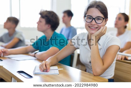 Teenager students sitting at desks and listening. Girl sitting in foreground and smiling. Royalty-Free Stock Photo #2022984980