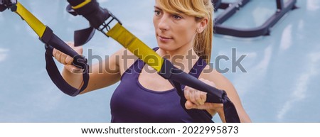 Portrait of beautiful woman doing hard suspension training with fitness straps in the gym