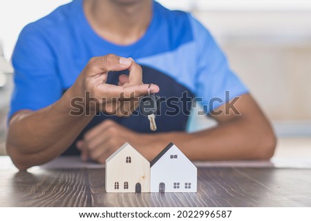 male hand holding a key, miniature wooden house and real estate business ideas
