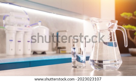there is a decanter and a glass of clean water on the kitchen table. in the background water filtration system Royalty-Free Stock Photo #2023023107
