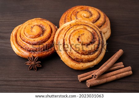 Three cinnamon buns on wooden table with some cinnamon sticks. Tasty homemade bakery