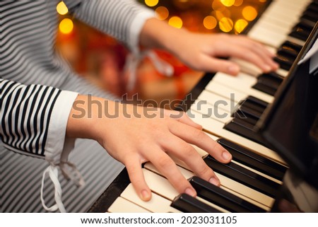Hands of young pianist on the piano, close up, Christmas lights on the background. Concept of winter holidays decoration and music.