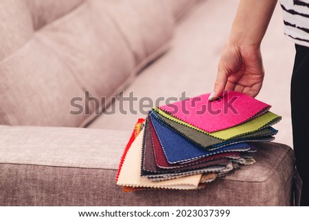 Woman chooses the colors and patterns of upholstery fabrics. Textile industry background. Tissue catalog. Young woman chooses the fabric for new sofa. Fabric samples to upholstery the sofa. Royalty-Free Stock Photo #2023037399