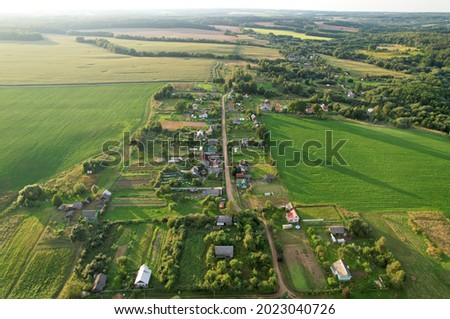 Top view of the village with wooden houses in wild among the forest and field. Aerial view of country house in countryside. Roofs of suburban homes. Housing outside the city in an ecological area.
