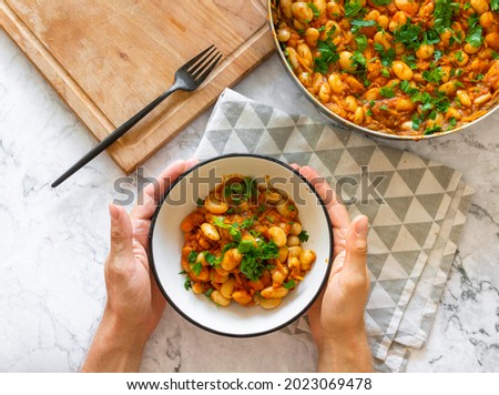 Tomato lobio of white bean pods and herbs in a bowl on a marble background. Lenten dish. Flat lay, top view thaditional georgian dish