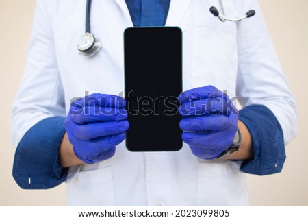 Midsection Of Doctor Holding Mobile Phone Against Plain Background