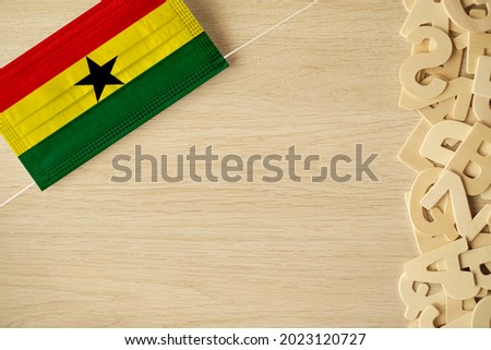 Ghana flag on hygienic mask. Rustic background with empty space. Top view.