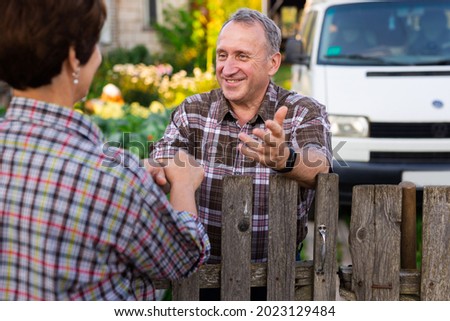 neighbors middle aged man and woman chatting near the fence in the village Royalty-Free Stock Photo #2023129484
