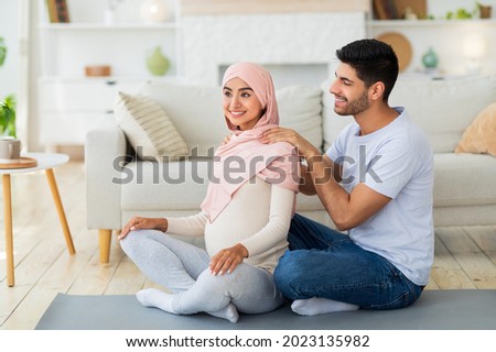 Loving arab husband massaging his expectant wife's shoulders at home, sitting together on floor. Tender man giving massage to his lovely wife to relieve tension during pregnancy Royalty-Free Stock Photo #2023135982