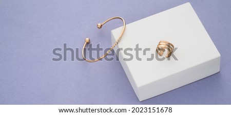 Panoramic shot of gold bracelet and ring on white box on purple background